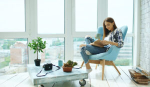 chica descansando leyendo un libro en el salón de su casa junto a la ventana